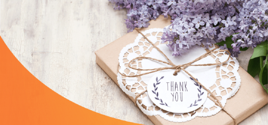 A gift with a Thank You greeting card and a bunch of purple flowers beside it