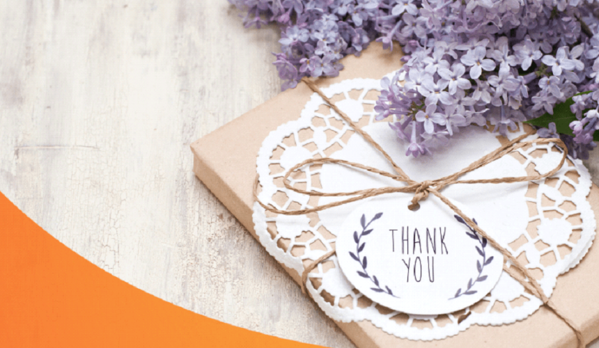 A gift with a Thank You greeting card and a bunch of purple flowers beside it